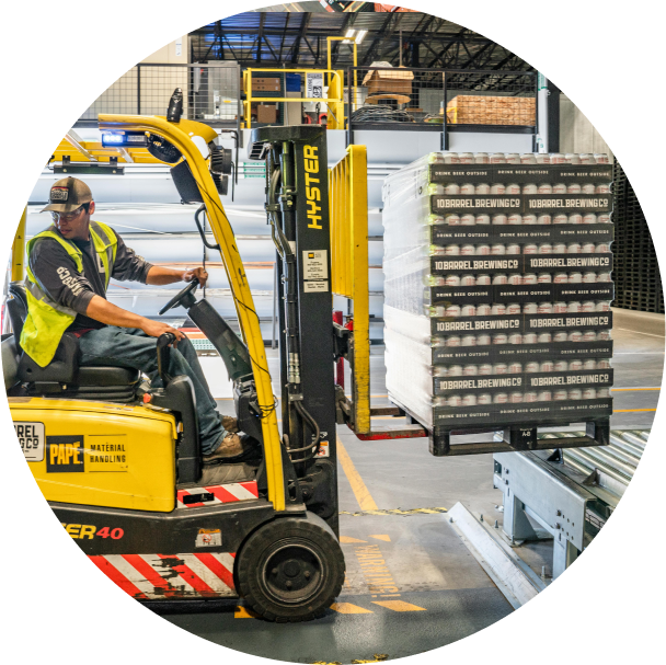 A worker operating a forklift, moving a pallet of boxed products in a warehouse or distribution center.